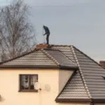 spazzacamino da lontano su un tetto ulisce un comignolo un'albero sullo sfondo