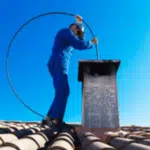 spazzacamino vestito di blu con scovolo pulisce una canna fumaria dal tetto